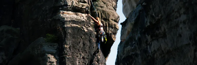 Grimpeur ascendant une falaise rocheuse avec paysage de montagne