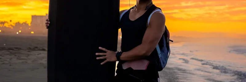 Surfeur marchant sur la plage au coucher du soleil avec sa planche sous le bras