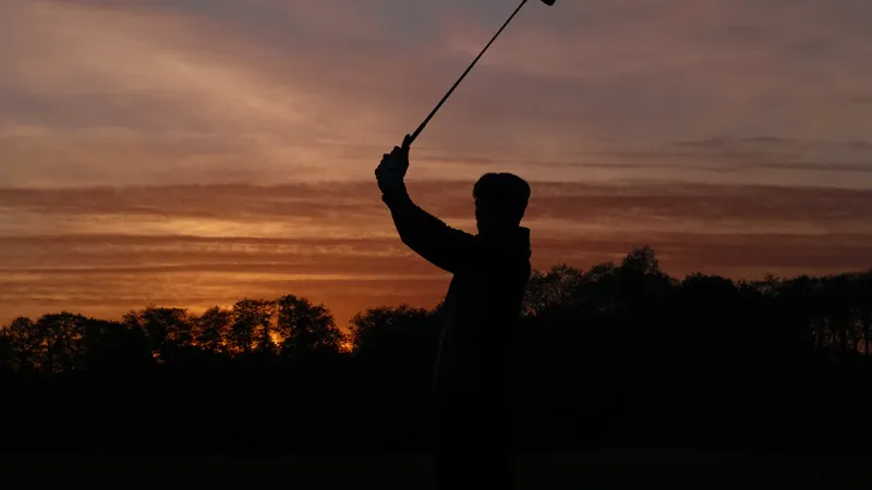 Moniteur de golf ramassant des balles sur le practice au coucher du soleil