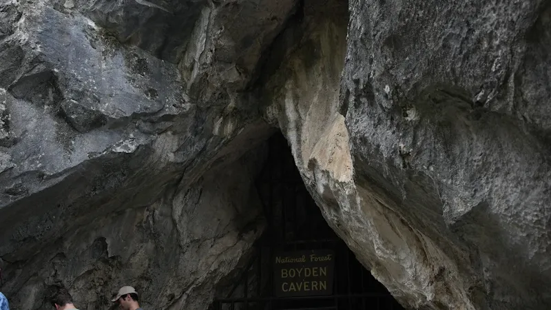 Guide spéléo équipant un participant devant l'entrée d'une grotte