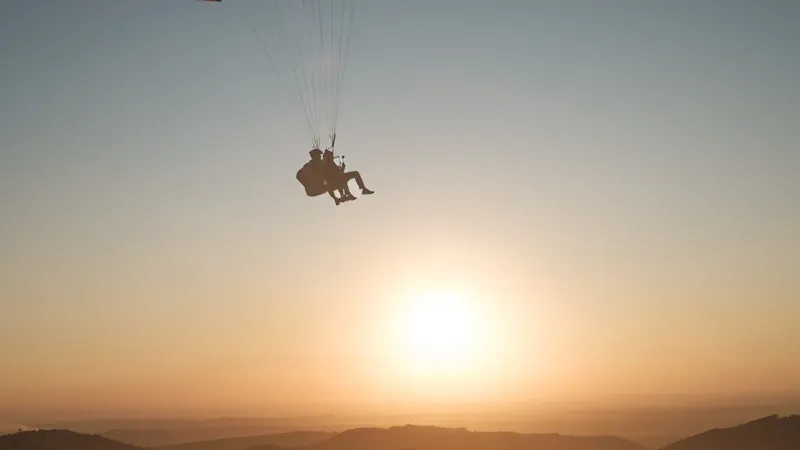 Vol biplace en parapente au coucher du soleil au-dessus des montagnes