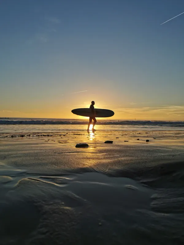 Surfeur marchant sur la plage avec sa planche au coucher du soleil
