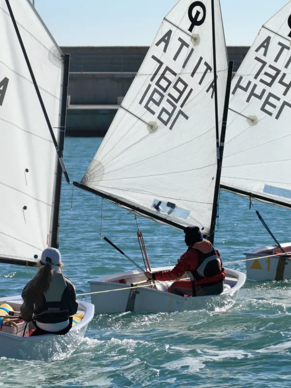 Enfants en gilets de sauvetage gréant un Optimist sur la plage