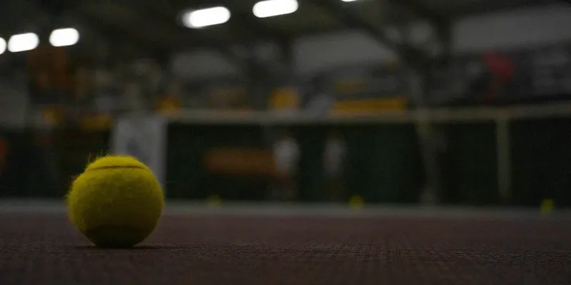 Panier de balles et raquettes posées sur un banc au bord du court